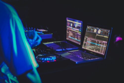 DJ performing with a laptop and mixing controller while digital DJ software is displayed on the screen.
