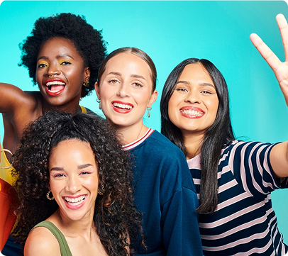 Four diverse women smiling and posing together for a cheerful group selfie against a turquoise background.
